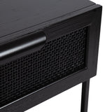 Close-up of a matte black wooden table corner featuring a woven cane panel drawer and a rounded wooden handle, supported by slender metal legs.