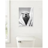 Black and white photo of a capybara wrapped snugly in a towel, hung above a white toilet in a bright bathroom with a window on the left.
