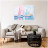 Abstract framed painting of sailboats with pastel pink and blue sails over a calm harbor, hung above a light gray sofa with a textured blanket and round pillow.