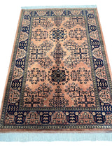 Traditional hand-knotted Bukharayi rug with peach field, intricate geometric dark blue patterns, bordered by a navy blue band with repeating motifs, finished with white fringes.