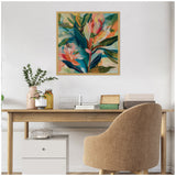 Abstract botanical painting with blue, green, coral, and peach leaves in a light wood frame, hanging above a minimalist desk with plants and books.