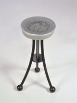 Small stool with a smooth, round, textured gray resin seat and three curved black metal legs each ending in a round ball foot, shown on a white background.
