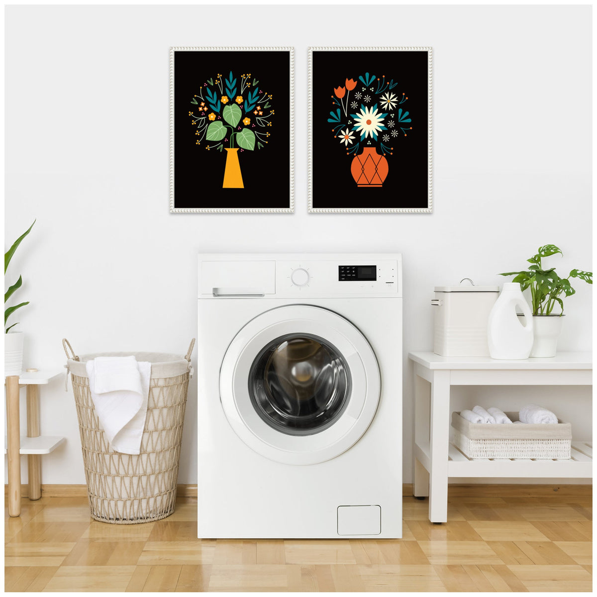 Two framed floral prints above a white front-loading washer, featuring yellow and red vases with stylized blue, white, and orange flowers on black backgrounds in a bright laundry room.