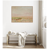 Muted landscape painting with soft beige, pink, and green tones hanging above a wooden bench with a light fabric throw and an open book in a bright, minimalist room.