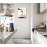 Bright kitchen with grey stone countertops, white cabinetry, and a framed canvas of a mother and baby giraffe in a pink bathtub on black-and-white checkerboard floor.