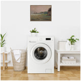 Laundry room with a white front-loading washing machine centered between a woven laundry basket and a small table holding a potted plant and cleaning supplies, under a framed landscape painting.