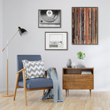 Contemporary living room corner with a blue armchair featuring wooden arms and a chevron pillow, next to a mid-century modern wooden sideboard under framed record-themed artwork.