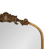 Top corner of an arched mirror with an ornate gold frame featuring intricate carved scrollwork and a smooth curved edge.