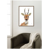 Framed canvas print of a stylized buck with large expressive eyes and textured antlers, hanging above a dark green armchair draped with a beige knit blanket.