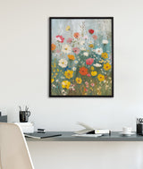 Framed colorful wildflower garden painting with yellow, white, pink, and orange flowers against a blue-gray background, hanging above a minimalist office desk.