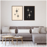 Two framed mid-century modern starburst art prints above a gray sectional sofa with striped and solid pillows, paired with light wood nested coffee tables on white floor.