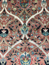 Close-up of a hand-knotted wool rug with intricate floral and vine patterns in red, blue, green, and cream tones forming a symmetrical design.
