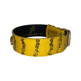 Mustard yellow dog collar with black snake-like stripes and textured scales, featuring metal buckle and black inner lining with gold logo text.