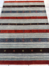 Hand-knotted rug with alternating horizontal stripes in rust, dark brown, and shaded blue, featuring small geometric and floral motifs across each stripe.