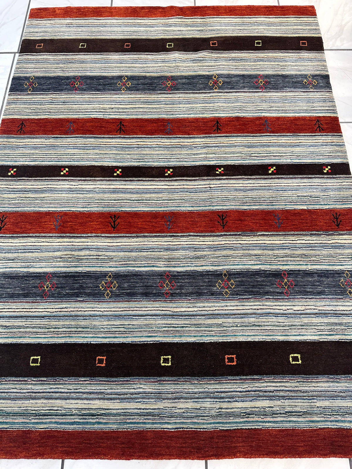 Hand-knotted rug with alternating horizontal stripes in rust, dark brown, and shaded blue, featuring small geometric and floral motifs across each stripe.