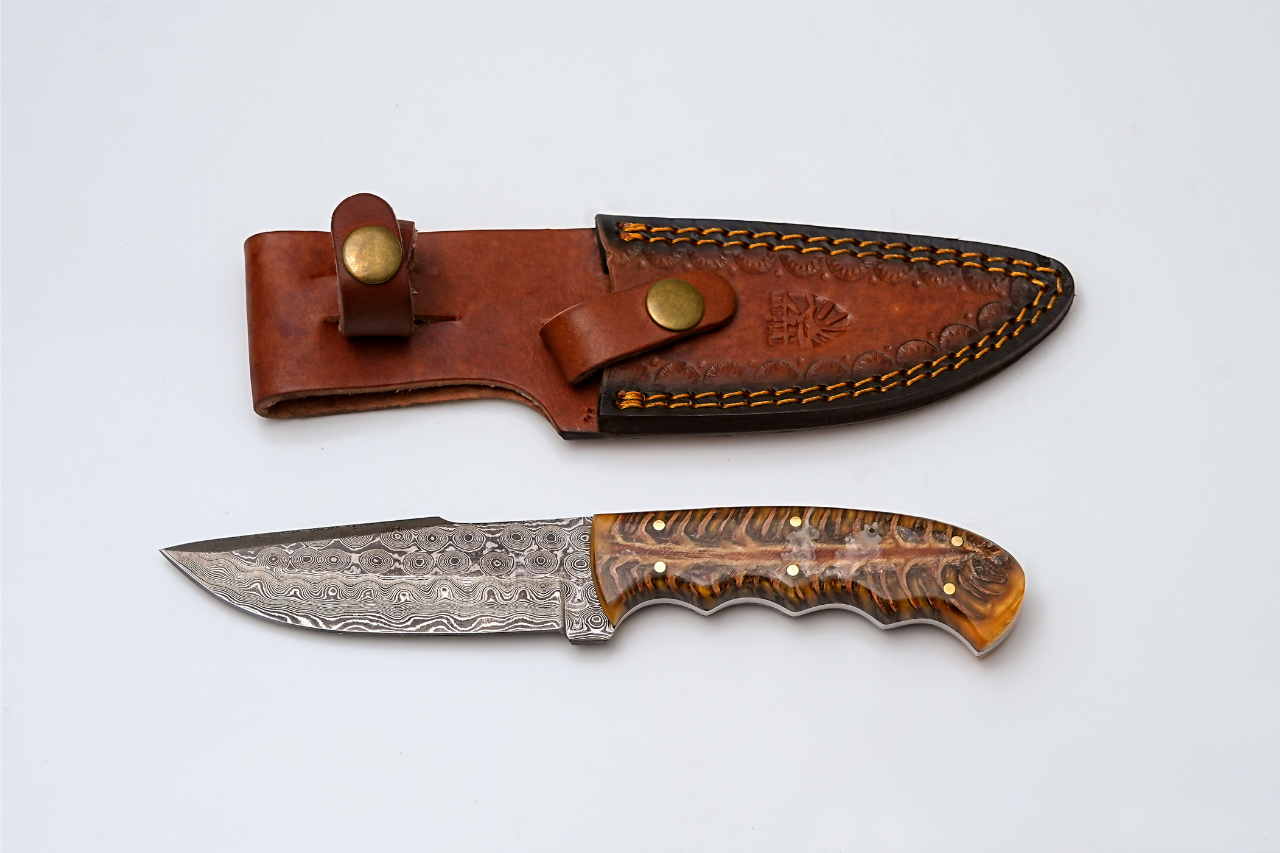 Handmade Damascus Steel "Titan Gecko" Fixed Blade Knife with amber resin handle set on a white textured surface