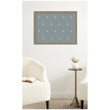 Rectangular blue pinboard with small white botanical block prints evenly spaced, framed in light wood, hanging on a white wall above two white textured chairs and a brass side table with a white vase.
