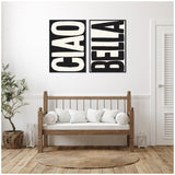 Two black and white framed canvases with large bold letters reading 'CIAO' and 'BELLA' hung side-by-side above a wooden bench with white cushions in a minimalist room.