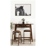 Black and white close-up photo of a horse's face with flowing mane, framed in wood and hung above a wooden bar table with two matching stools.