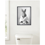 Black and white framed canvas of a bunny wearing a white bathrobe, displayed on a white bathroom wall above a toilet.