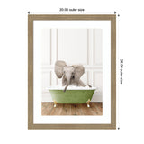 Baby elephant sitting in a green clawfoot bathtub with white foam, set against white paneled walls and a wooden floor, framed in light wood.