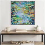 Abstract impressionist painting of water lilies with vibrant greens, blues, yellows, and pink accents in a gray frame above a wood and metal console table.