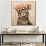Painting of a brown tabby cat with green eyes wearing a colorful floral crown, hung above a wood and metal console table with books, a cup, and a white vase with greenery.