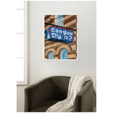 Framed canvas print showing a blue vintage-style sign reading 'Can you Dig it?' hanging on a brick building with arched windows, displayed above a dark green armchair and beige knitted throw.