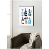Framed wall art showing six artistic blue-toned champagne and wine bottles with decorative ribbons, hung above a dark olive armchair draped with a cream knitted throw.