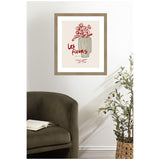 Framed wall art featuring a red floral line drawing in a striped vase with the text 'Les Fleurs' in red on a beige background, displayed above a dark green sofa and next to a potted olive tree.