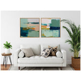 Two framed abstract canvas art pieces with teal, peach, navy, and white blocks above a white sofa with patterned and solid pillows flanked by green plants.