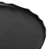 Close-up of a black round tray with irregular wavy edges and a slightly textured surface.