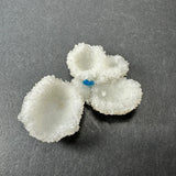 Four white, cup-shaped stilbite mineral formations with crystalline surfaces, featuring a small bright blue cavansite ball nestled among them on a dark gray background.