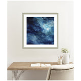 Abstract artwork with rich blue and dark teal watery patterns, accented by light blue highlights and subtle white veining, framed in neutral-toned molding above a wooden desk.