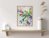 Framed botanical print with jewel-toned leaves and red blossoms in shades of green, yellow, and blue on a light background, displayed above a wooden shelf with vases.