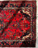 Red Persian Hamadan wool rug with intricate floral and geometric patterns in black, cream, and green, featuring multiple detailed borders and fringed edges.