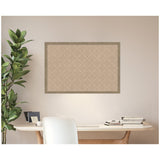 Beige pinboard with a subtle lattice pattern framed in light wood, hanging above a modern desk with books and a white chair, next to a tall leafy plant.