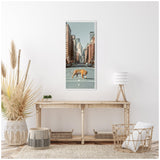 Framed vertical canvas of a tiger walking across a city street lined with tall buildings, displayed on a white wall above a rustic wooden console with neutral decor.