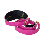 Bright pink leather belt with gold buckle and black underside, coiled with visible stitching and small holes for adjustment.