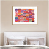 Abstract grid artwork with rectangular patches in shades of pink, red, purple, and orange, each featuring varied abstract patterns, framed and hung above a bed.