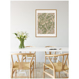 Dining room with light wood chairs around a white table, featuring a William Morris Windrush 1883 framed botanical print and a vase of white calla lilies.