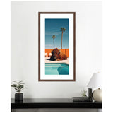 Framed photo of a bison lounging near a light blue pool with an orange wall and two tall palm trees against a clear blue sky.