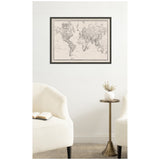 Black and white vintage-style world map printed on textured linen fabric, framed and hung on a white wall above a small round brass side table between two cream upholstered chairs.