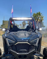 Front view of a black Polaris Pro R RZR with a bright LED light bar mounted on the roof and two American flags on antennae at the rear corners