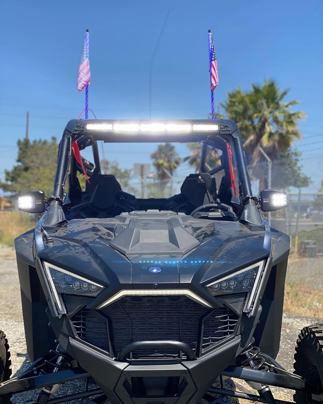 Front view of a black Polaris Pro R RZR with a bright LED light bar mounted on the roof and two American flags on antennae at the rear corners