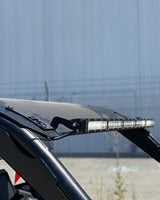Black 30-inch roof mount securely attached to a Polaris Pro R RZR, holding a long LED light bar above the vehicle's windshield frame against a blue industrial wall background.