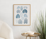 Framed abstract print of various blue coral-inspired shapes arranged in a grid on a white wall above a brass round table and near a green plant.