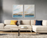 Living room with a beige sectional sofa featuring yellow, gray, pink, and navy pillows, a light wood oval coffee table, and two framed abstract ocean paintings with blue and orange tones on the wall.