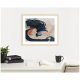 Abstract artwork with deep blue, soft peach, and beige brushstrokes in a light wood frame above a white desk with an open book, black cup, and green plant.