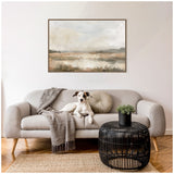 Light gray sofa with a gray throw and round pillow, a black round wicker coffee table with a small green plant, and a framed neutral-toned abstract landscape painting on the wall, with a white and brown dog sitting on the sofa.